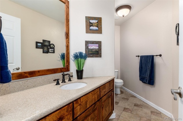 bathroom with toilet, baseboards, stone finish floor, and vanity