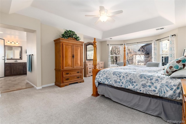 bedroom with a tray ceiling, light colored carpet, visible vents, a sink, and baseboards