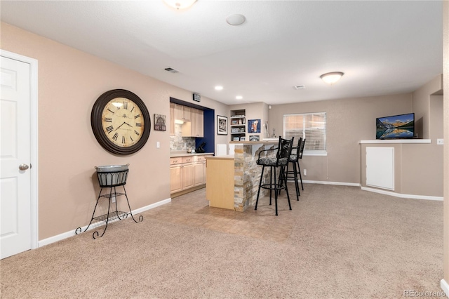 kitchen with light brown cabinets, light carpet, visible vents, a kitchen breakfast bar, and light countertops