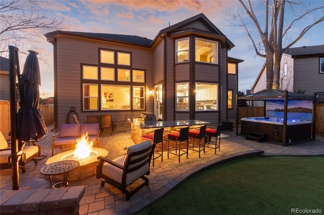 back of house at dusk featuring a fire pit, a patio area, fence, and a hot tub