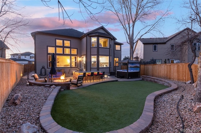 back of house at dusk featuring a patio area, an outdoor fire pit, a lawn, and a fenced backyard