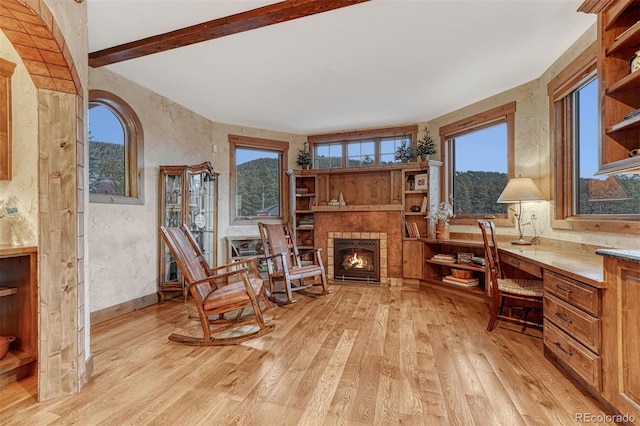 living area with a wealth of natural light, built in desk, beam ceiling, and light wood-type flooring