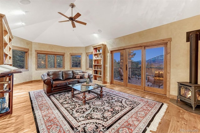 living room featuring light hardwood / wood-style flooring, vaulted ceiling, ceiling fan, and a wood stove