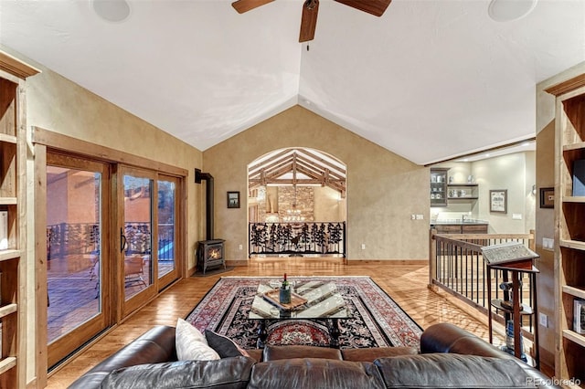 living room featuring vaulted ceiling, a wood stove, ceiling fan, and light hardwood / wood-style flooring