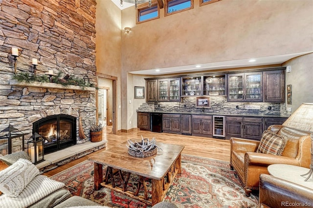 living room with wine cooler, bar, a stone fireplace, and light wood-type flooring