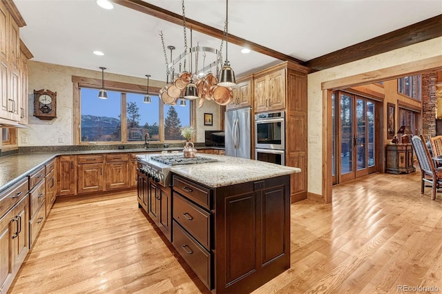 kitchen with hanging light fixtures, beam ceiling, stainless steel appliances, and light hardwood / wood-style floors