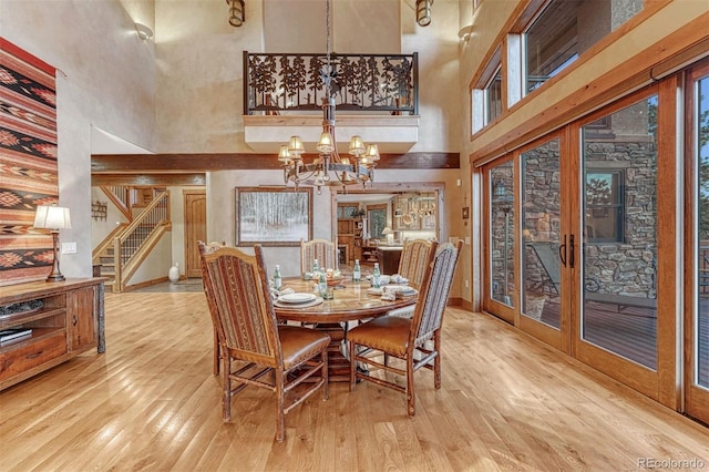 dining space featuring french doors, an inviting chandelier, light wood-type flooring, a towering ceiling, and a healthy amount of sunlight