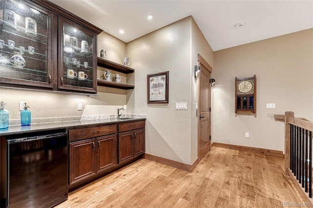 bar with dark brown cabinets, dark stone counters, black dishwasher, and light wood-type flooring