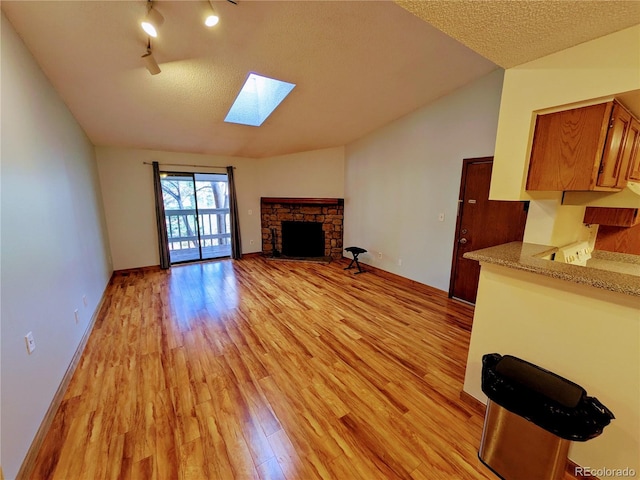 unfurnished living room featuring light wood-type flooring, a textured ceiling, lofted ceiling with skylight, and a stone fireplace