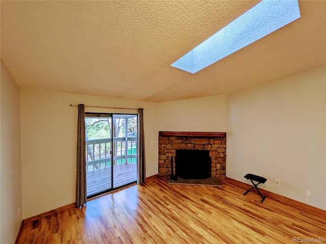 unfurnished living room featuring light wood finished floors, a textured ceiling, a stone fireplace, baseboards, and a skylight