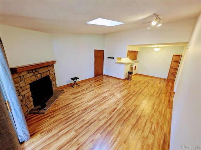 unfurnished living room featuring a stone fireplace, a skylight, baseboards, track lighting, and light wood-style floors