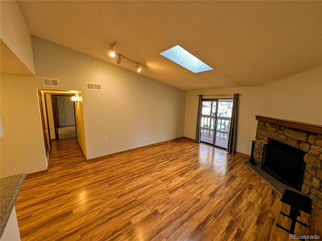 unfurnished living room with visible vents, lofted ceiling with skylight, wood finished floors, and a stone fireplace