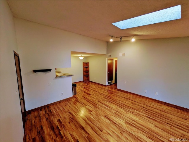 empty room with baseboards, rail lighting, light wood-style flooring, and a skylight