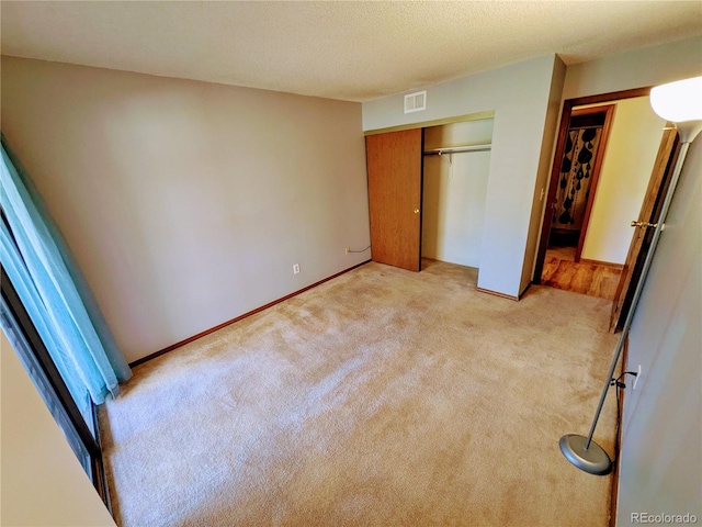 unfurnished bedroom featuring a closet, light colored carpet, a textured ceiling, and visible vents