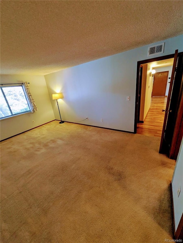 spare room featuring baseboards, carpet, a textured ceiling, and visible vents