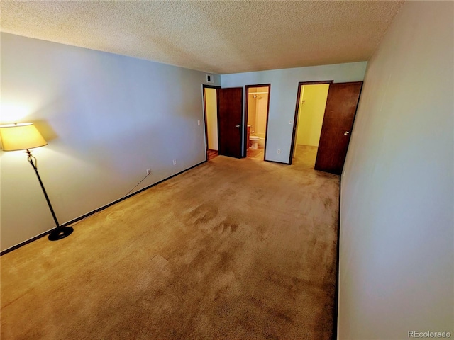 unfurnished bedroom with carpet floors, ensuite bath, and a textured ceiling