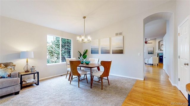 1229 Berganot Trl, Castle Pines, CO 80108 - dining space with arched walkways, a chandelier, a glass covered fireplace, baseboards, and light wood-style floors