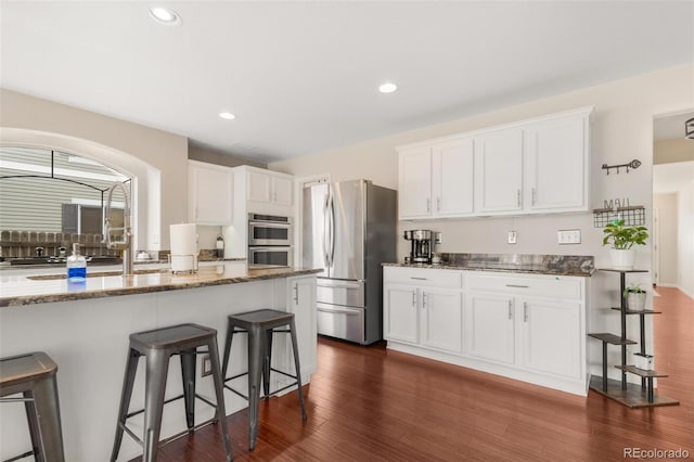 11885 Helena St, Commerce City, CO 80022 - kitchen featuring appliances with stainless steel finishes, white cabinetry, a breakfast bar area, dark stone counters, and dark wood-type flooring