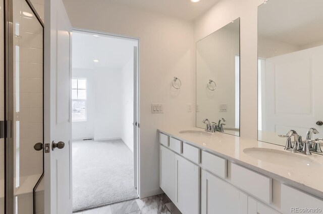 bathroom featuring double vanity, walk in shower, a sink, and baseboards