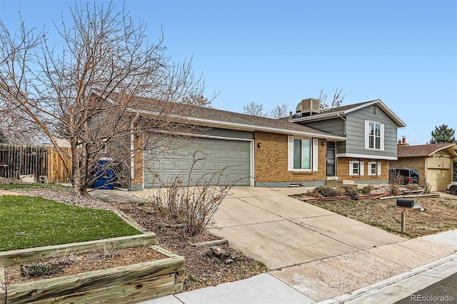 split level home with concrete driveway, roof with shingles, an attached garage, brick siding, and fence