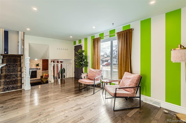 living area featuring recessed lighting, wood-type flooring, visible vents, and a brick fireplace