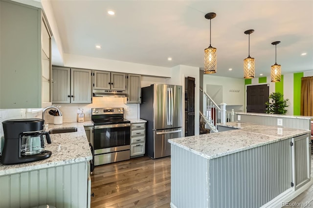 kitchen with a sink, appliances with stainless steel finishes, under cabinet range hood, wood finished floors, and decorative backsplash