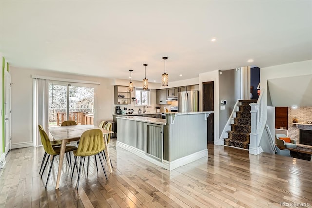 kitchen with light wood-style floors, open shelves, a kitchen island, appliances with stainless steel finishes, and hanging light fixtures