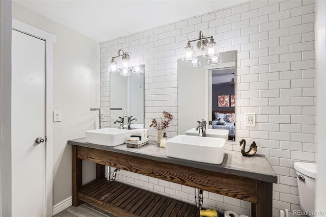 bathroom with a sink, tile walls, double vanity, and toilet