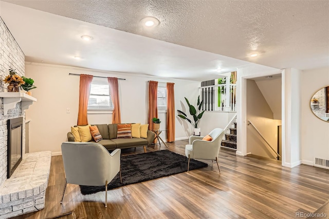 living room featuring a textured ceiling, visible vents, wood finished floors, a brick fireplace, and baseboards