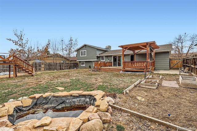 back of house with a deck, a fenced backyard, and a vegetable garden