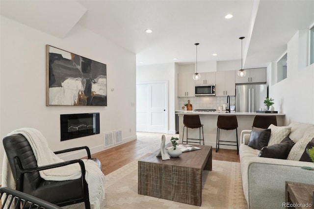 living room featuring baseboards, visible vents, recessed lighting, a glass covered fireplace, and light wood-type flooring