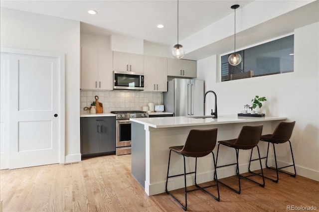 kitchen with light countertops, a kitchen bar, decorative backsplash, appliances with stainless steel finishes, and a sink