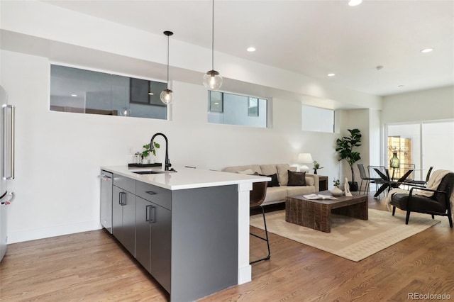 kitchen featuring light wood-style flooring, a peninsula, stainless steel dishwasher, and a sink