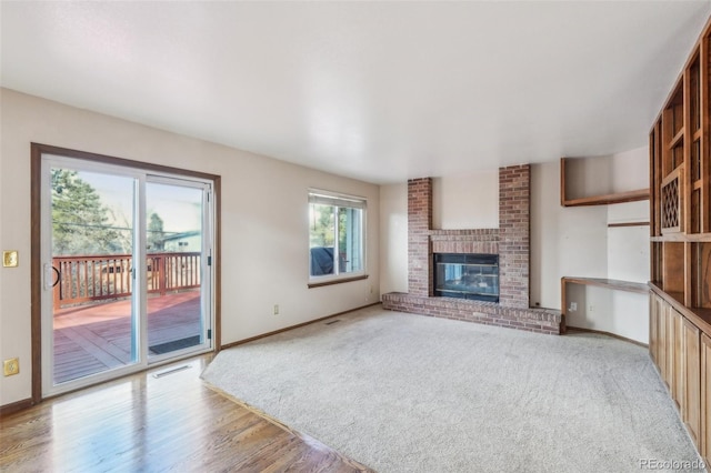 unfurnished living room with a brick fireplace, visible vents, light wood finished floors, and baseboards