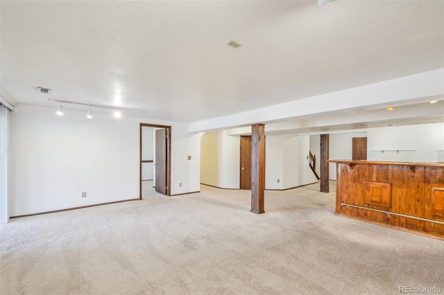 finished basement featuring light carpet, visible vents, baseboards, a bar, and rail lighting