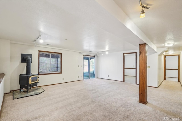 below grade area with carpet floors, a wood stove, and track lighting