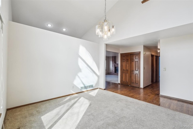 spare room featuring carpet floors, a notable chandelier, recessed lighting, visible vents, and a brick fireplace