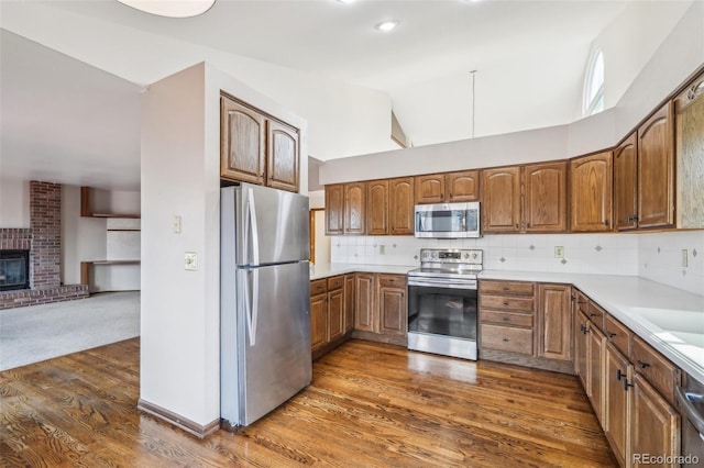 kitchen with appliances with stainless steel finishes, lofted ceiling, brown cabinetry, and tasteful backsplash