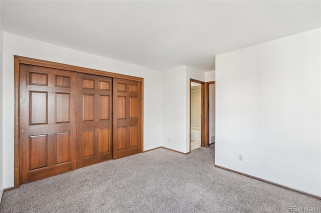 unfurnished bedroom featuring carpet, a closet, ensuite bath, and baseboards