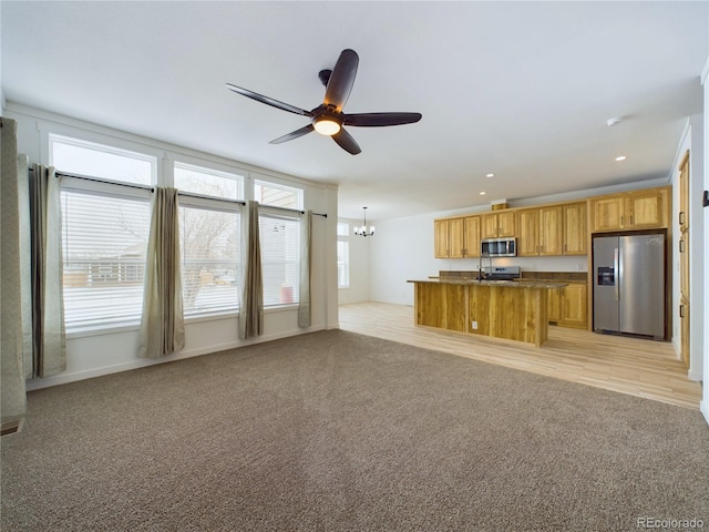 kitchen featuring an island with sink, appliances with stainless steel finishes, light colored carpet, and ceiling fan with notable chandelier