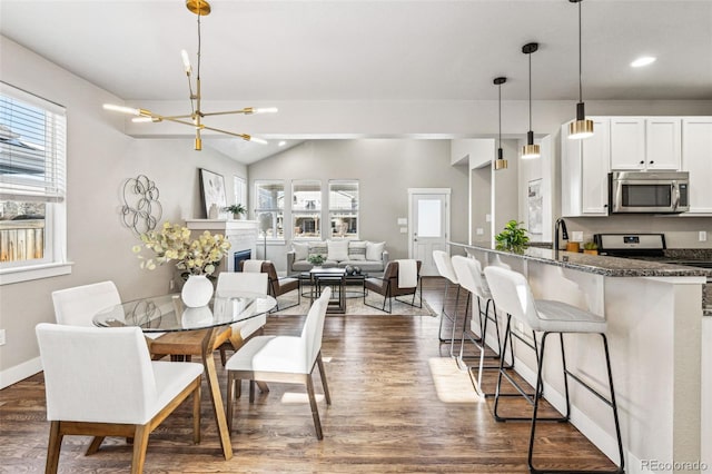 dining space with dark hardwood / wood-style floors, vaulted ceiling, and a notable chandelier