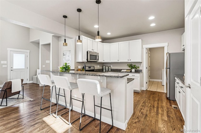 kitchen featuring stainless steel appliances, white cabinetry, dark hardwood / wood-style flooring, and dark stone counters