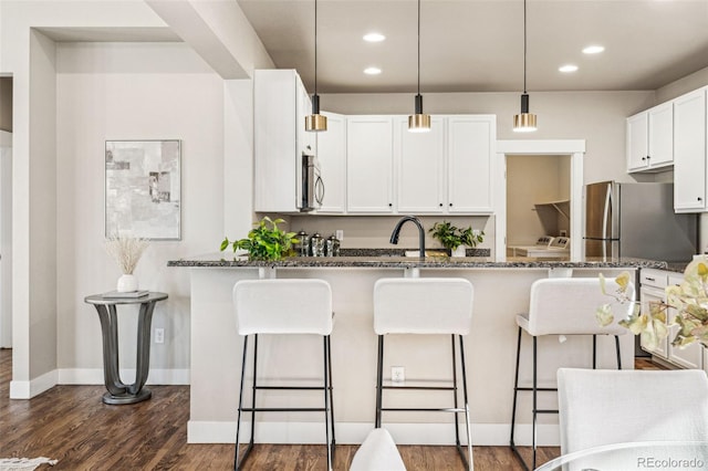 kitchen with white cabinets, a kitchen bar, dark stone counters, kitchen peninsula, and stainless steel appliances