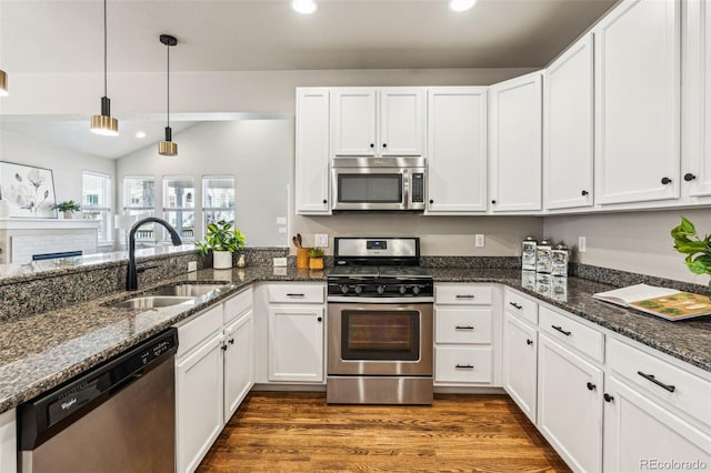 kitchen with sink, white cabinetry, stainless steel appliances, decorative light fixtures, and dark stone counters