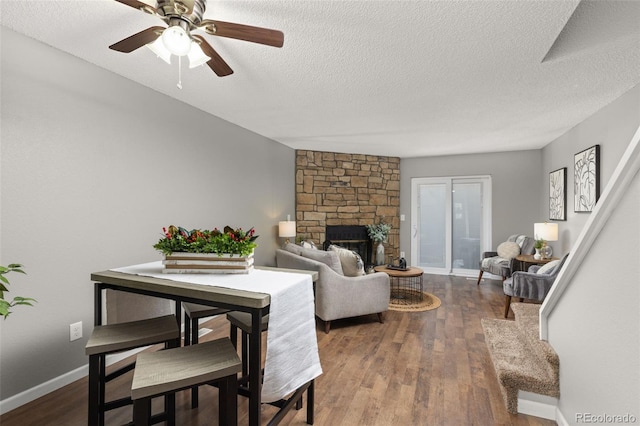 living room with a fireplace, a textured ceiling, dark hardwood / wood-style floors, and ceiling fan