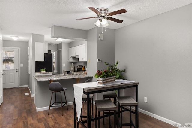 kitchen with kitchen peninsula, dark hardwood / wood-style flooring, black appliances, white cabinetry, and a breakfast bar area