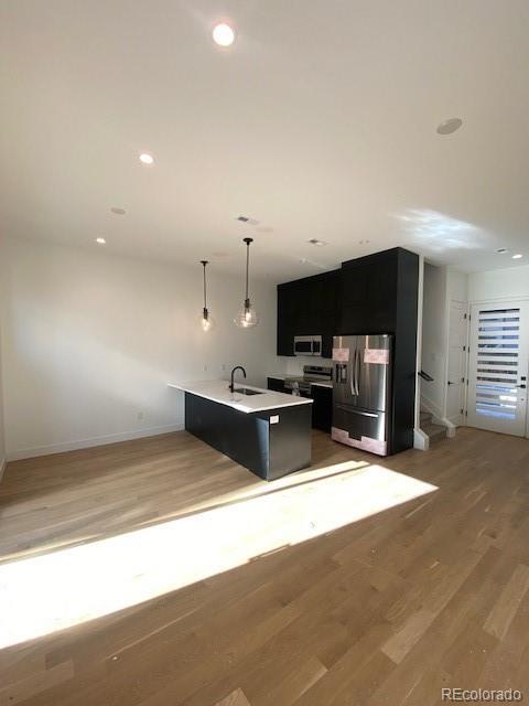 kitchen featuring stainless steel appliances, light countertops, a kitchen island with sink, a sink, and dark cabinets