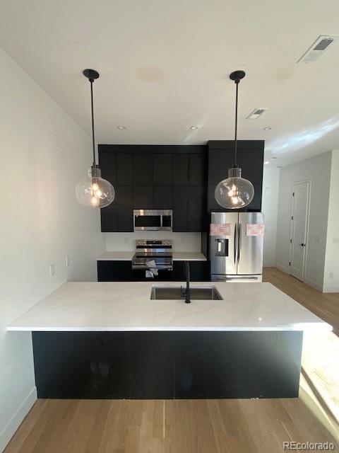 kitchen featuring visible vents, stainless steel appliances, light countertops, pendant lighting, and a sink