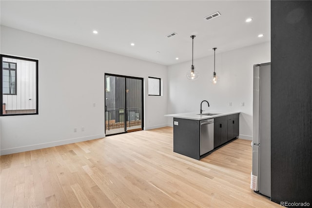 kitchen featuring light wood-style flooring, appliances with stainless steel finishes, decorative light fixtures, light countertops, and a sink