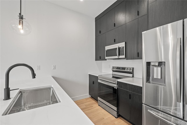 kitchen featuring dark cabinets, a sink, hanging light fixtures, appliances with stainless steel finishes, and light countertops